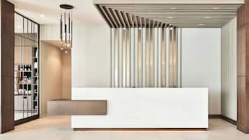 Un área de recepción moderna con un mostrador blanco, diseño vertical de listones en la pared y una lámpara colgante.