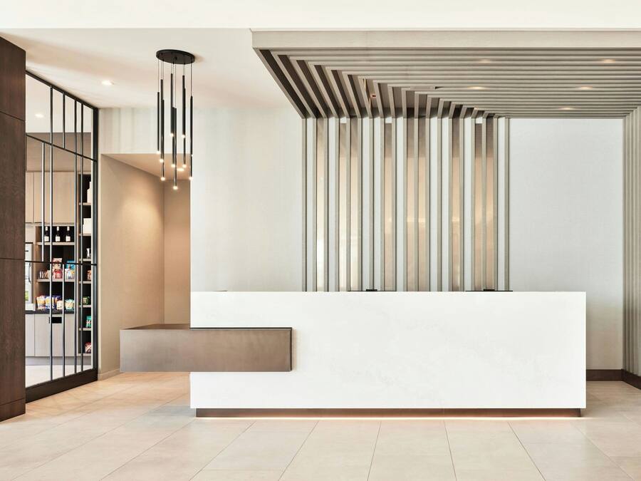 Un espace d’accueil moderne avec un comptoir de réception blanc, un motif vertical à lamelles sur le mur et un luminaire suspendu.