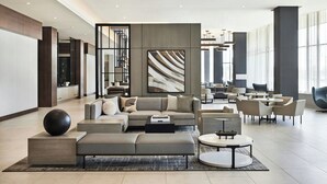 A spacious lobby with a sectional sofa, a coffee table, and a round table with chairs. There is a large abstract painting on the wall and a staircase in the background. - AC Hotel by Marriott St. Louis Chesterfield (Chesterfield)