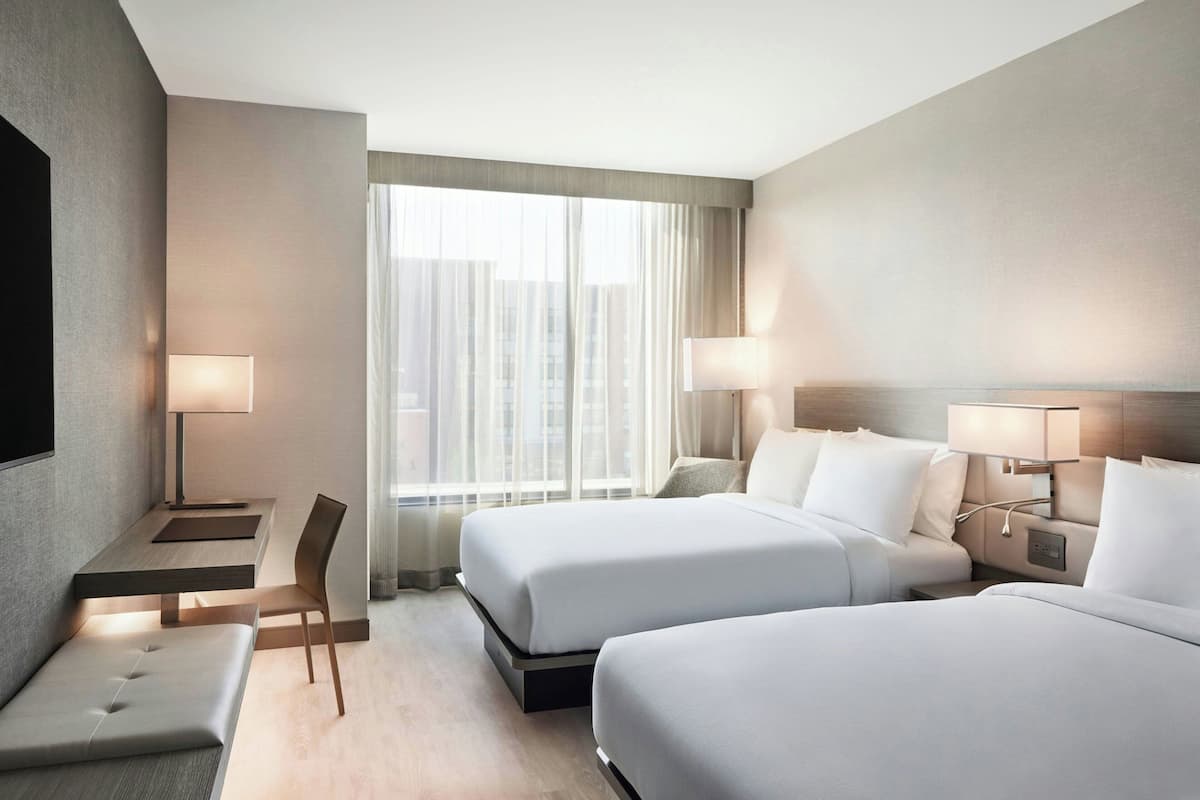 A hotel room with two beds, a desk, a chair, and a TV.