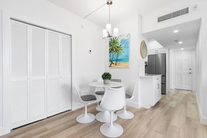 Eine moderne Küche mit weißen Schränken, einem Edelstahl-Kühlschrank und einem Essbereich mit rundem Tisch und weißen Stühlen.