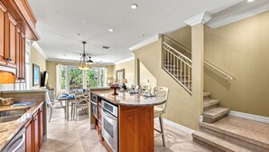 A spacious kitchen with a central island, wooden cabinets, and a dining area with chairs and a table. - Endless Views | Walking Distance To Siesta Key Beach + Village w/ Rooftop Panoramic Views! (Siesta Key)