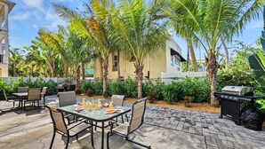 An outdoor patio with a table set for dining, surrounded by palm trees and a barbecue grill. - Endless Views | Walking Distance To Siesta Key Beach + Village w/ Rooftop Panoramic Views! (Siesta Key)