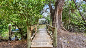 A wooden bridge leading to a building with a blue roof, surrounded by dense foliage. - Endless Views | Walking Distance To Siesta Key Beach + Village w/ Rooftop Panoramic Views! (Siesta Key)