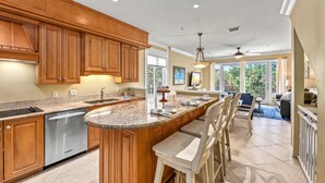 A spacious kitchen with wooden cabinets, a built-in island with bar stools, and a large window providing natural light. - Endless Views | Walking Distance To Siesta Key Beach + Village w/ Rooftop Panoramic Views! (Siesta Key)