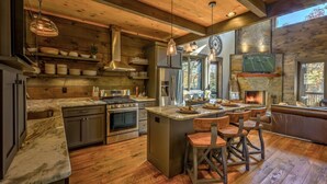 A rustic kitchen with wooden beams, a large island, and a fireplace. - Singing Pines - Mountain Views | Hot Tub | Screened Porch | Fire Pit (Blue Ridge)