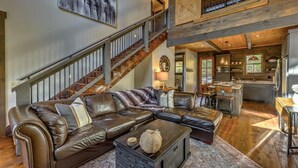 A spacious living area with a large leather sectional sofa, a staircase, and a kitchen area. - Singing Pines - Mountain Views | Hot Tub | Screened Porch | Fire Pit (Blue Ridge)
