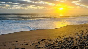 A beach with footprints leading to the water, a sunset, and a cloudy sky. - Oceanfront Luxury Townhome # 2• Private Beach & Pool Access Sleeps 8 (Melbourne Beach)