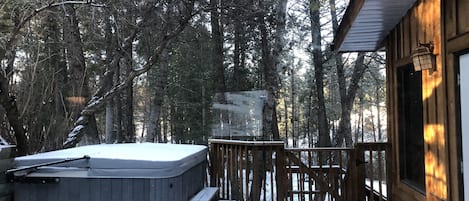 A wooden cabin with a hot tub on a deck surrounded by trees.