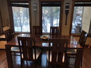 A dining area with a wooden table and chairs, large windows with a view of trees, and a paddle on the wall.
