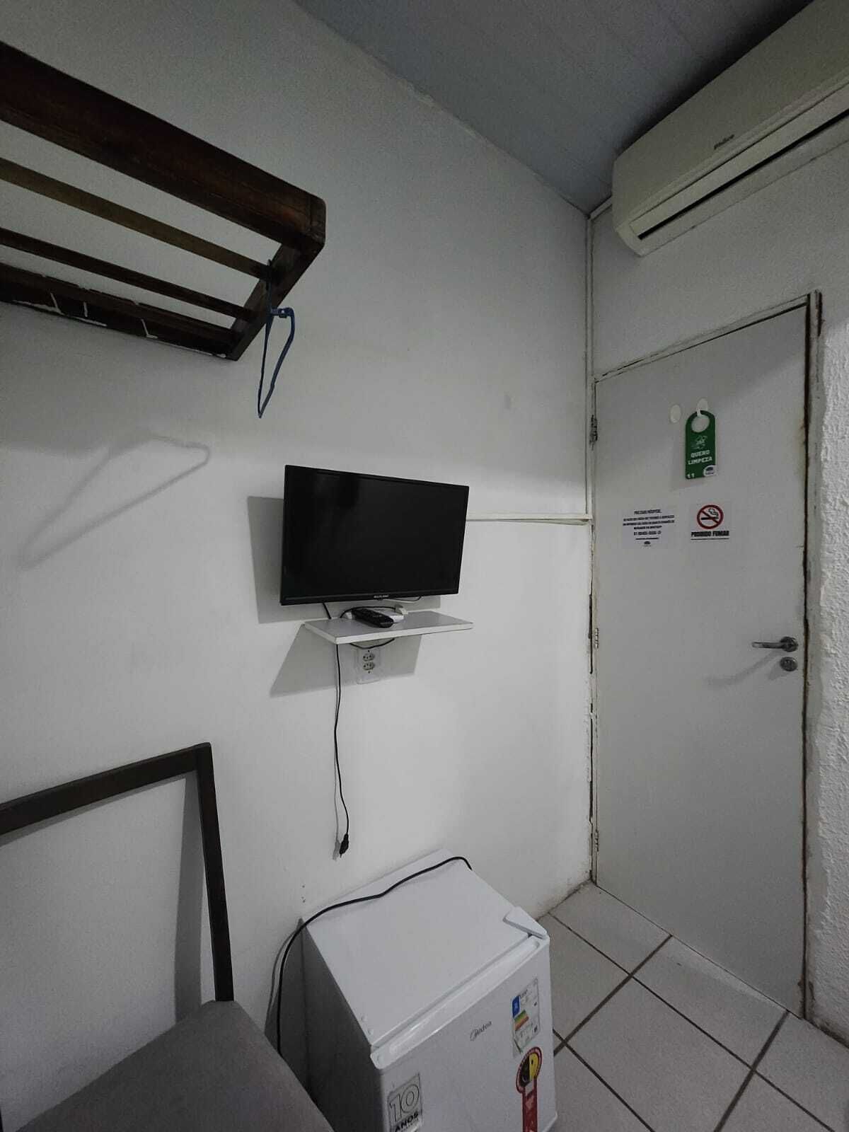 A small room with a television mounted on the wall, a white cabinet, and a door with a green sign.