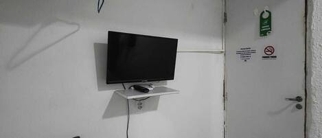 A small room with a television mounted on the wall, a white cabinet, and a door with a green sign.