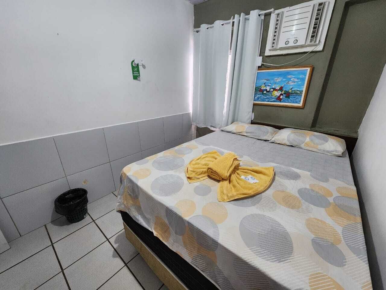 Hotellihuone, jossa on kaksi sänkyä, pieni roskakori, taulu seinällä ja ikkuna, jossa on verhot.