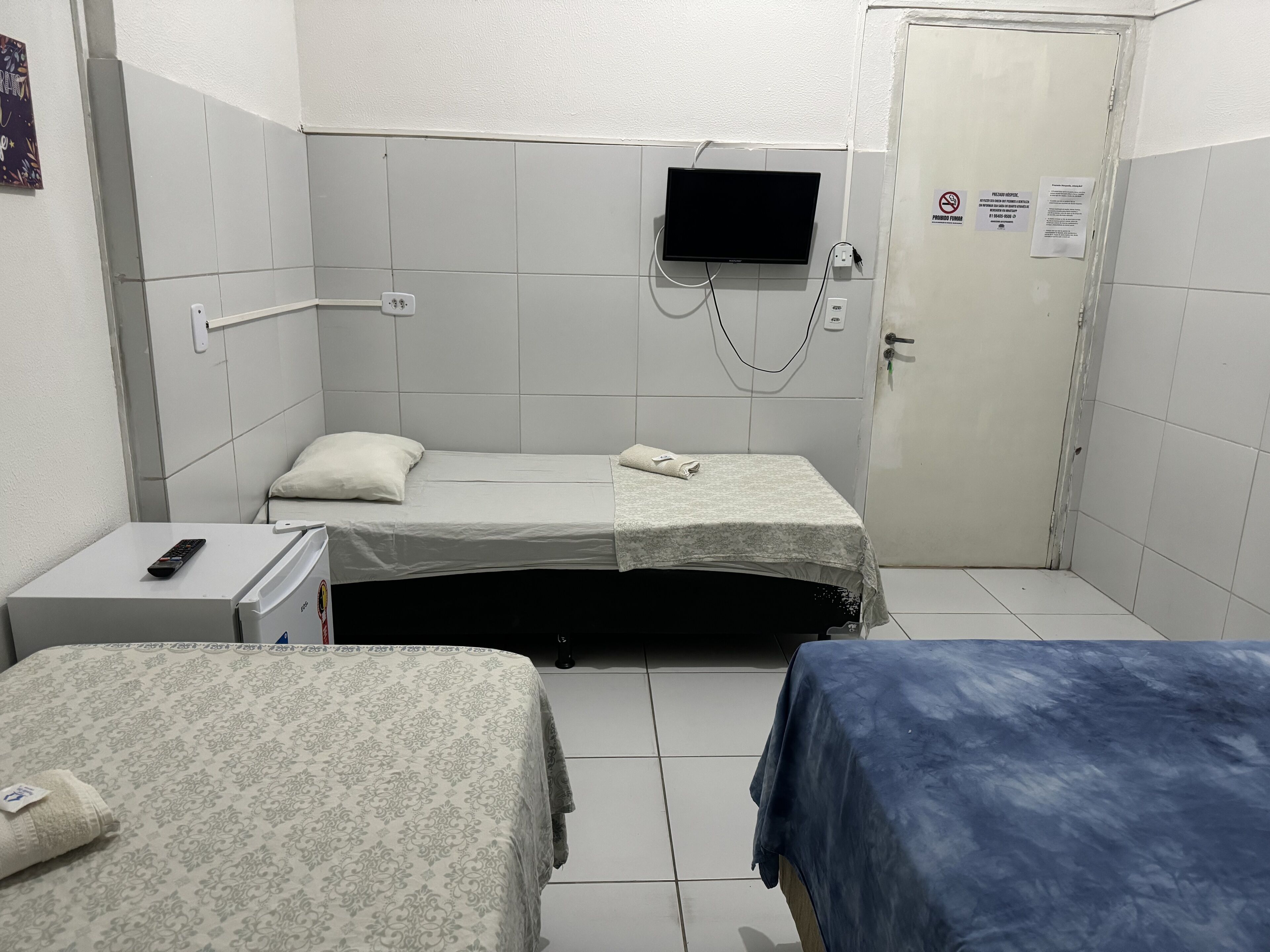 Una habitación pequeña y limpia con dos camas, un televisor en la pared y una puerta con un cartel.