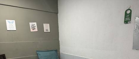 A small, single-bed room with a teal bedspread, a wooden chair, and three motivational posters on the wall.