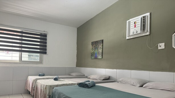 A hotel room with two beds, a window with blinds, a wall-mounted air conditioner, and a painting. - Casa Recife Pousada (Recife)
