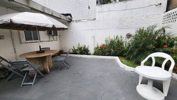 Un patio con una mesa redonda y sillas, una sombrilla blanca y una silla blanca.