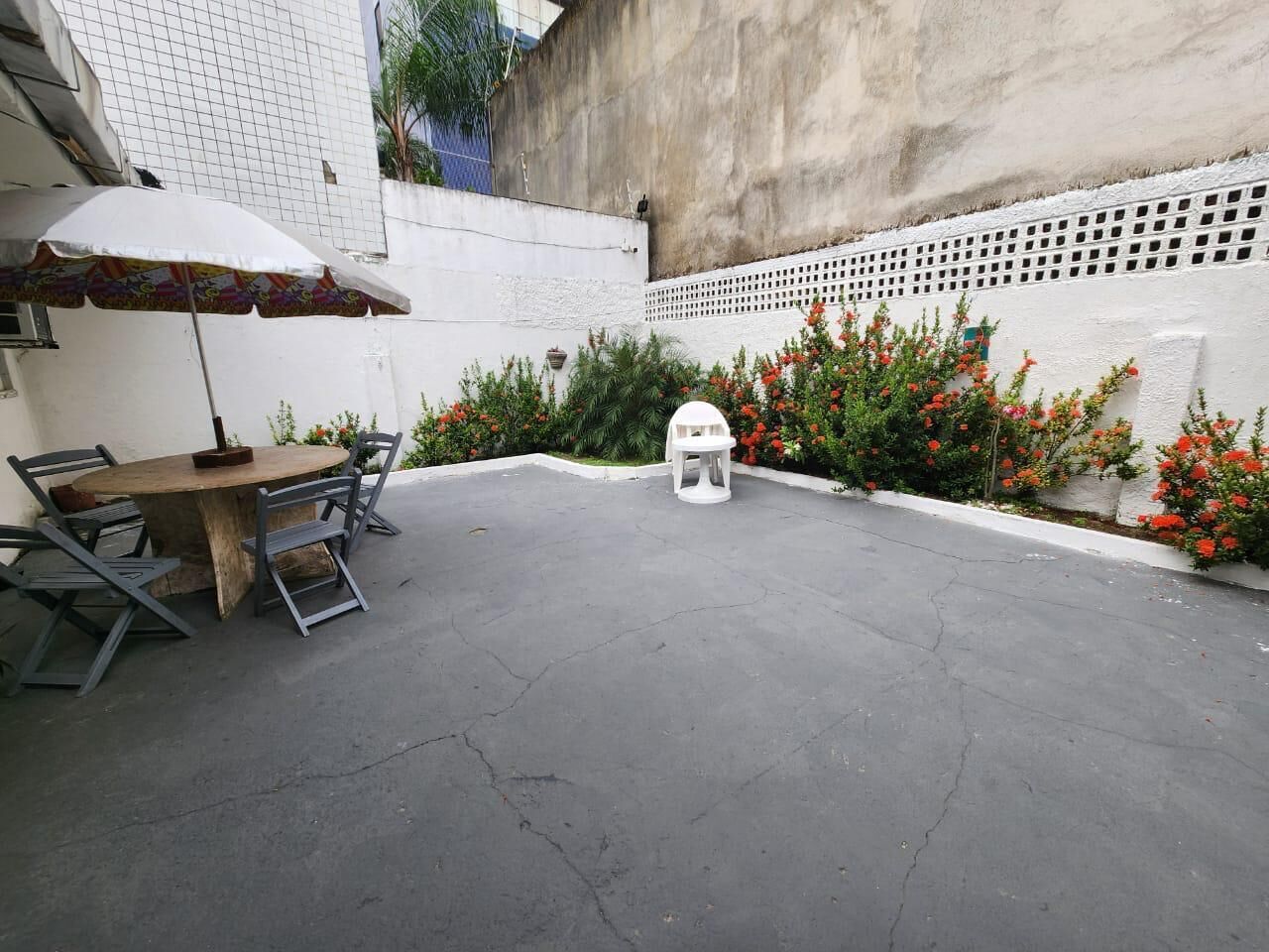 A courtyard with a round table and chairs, a small white stool, and a white umbrella.