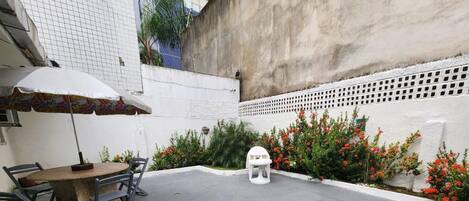 A courtyard with a round table and chairs, a small white stool, and a white umbrella.