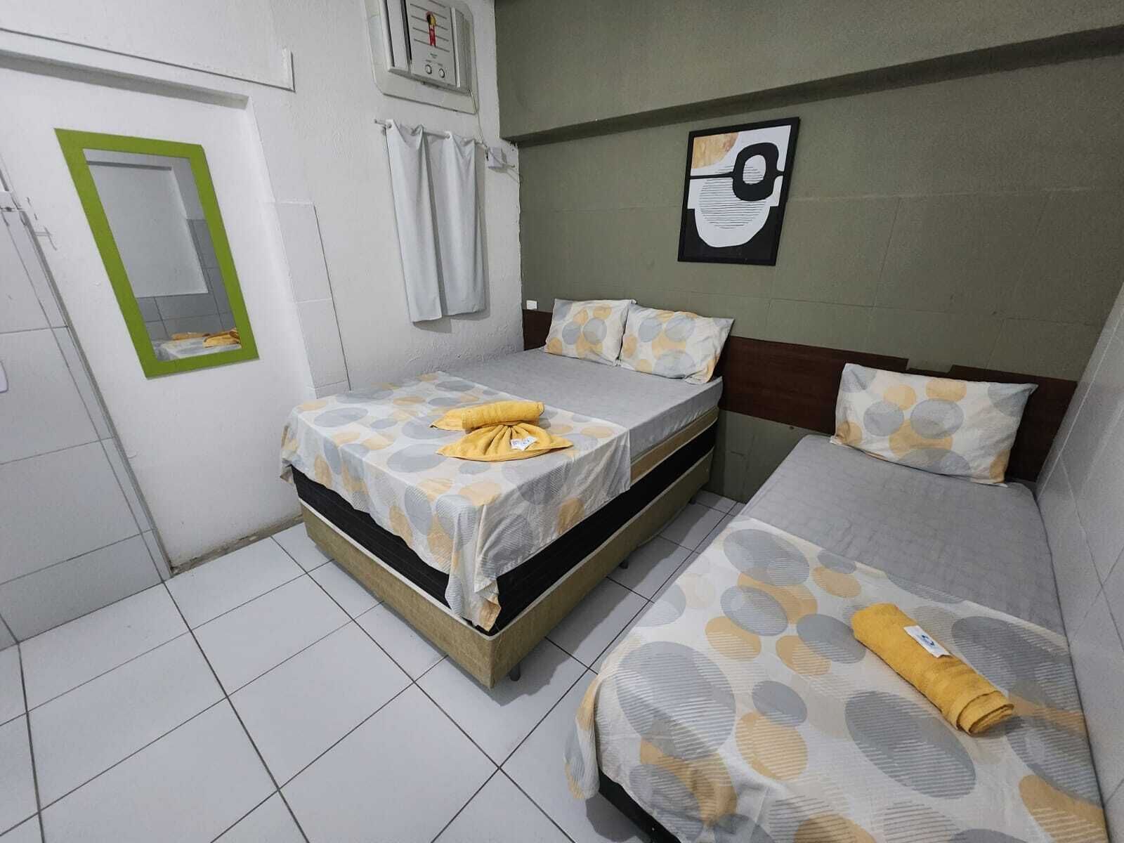 Une petite chambre propre, avec deux lits, un miroir et un thermostat fixé au mur.