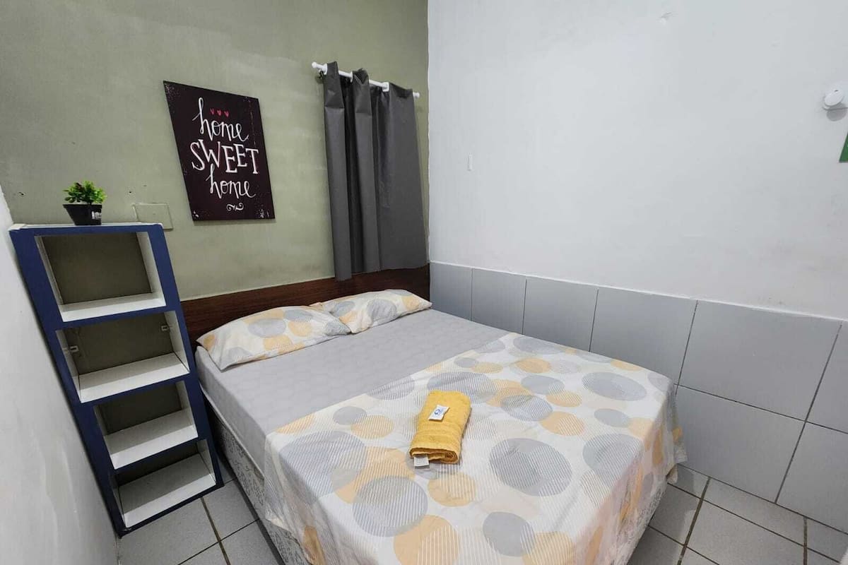 A small, neatly arranged bedroom with a bed, a shelf, and a sign on the wall.