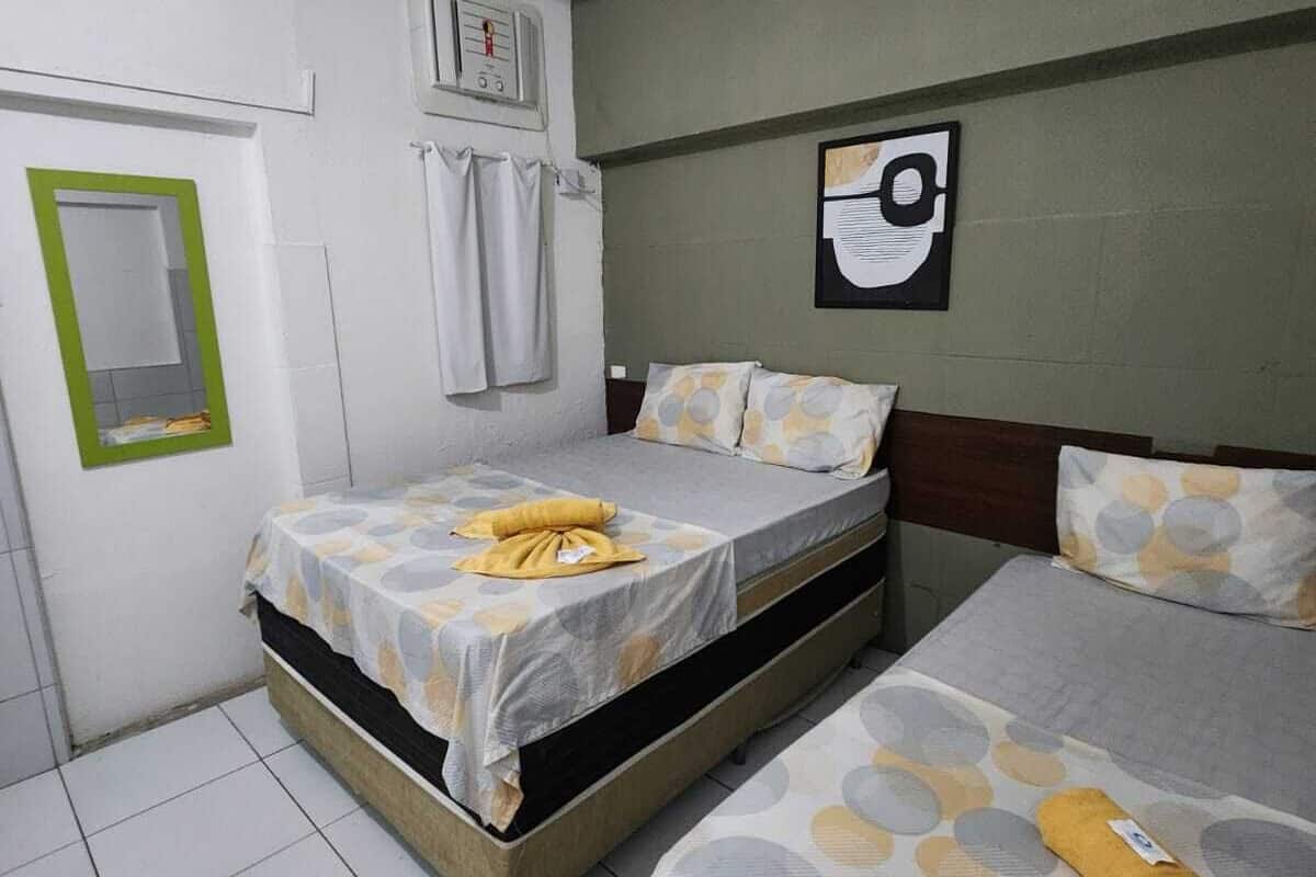A small, clean room with a bed, a chair, a small table, and a wall-mounted heater.