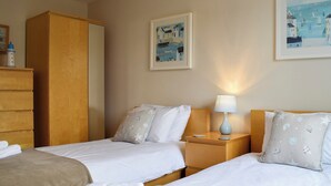 A hotel room with two beds, a wooden wardrobe, a bedside table with a lamp, and artwork on the walls.