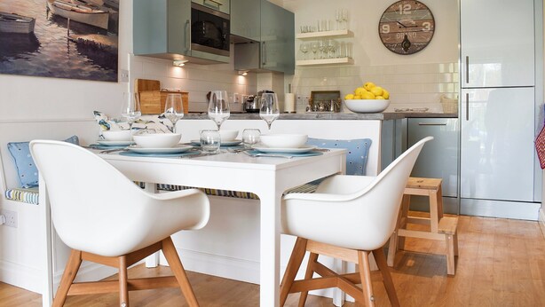 A modern kitchen with a central island, white chairs, and a dining table set for four.