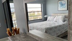 Een slaapkamer met een bed, een houten dressoir, een raam en uitzicht op de stad.