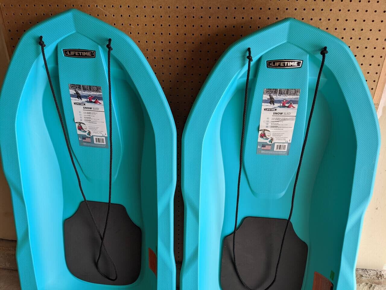 Two turquoise sleds with black handles and a black bag attached, labeled 'LIFETIME' and 'SNOW SLED'.