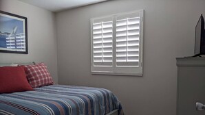 Un dormitorio con cama, cómoda, ventana con persianas e imagen enmarcada en la pared.