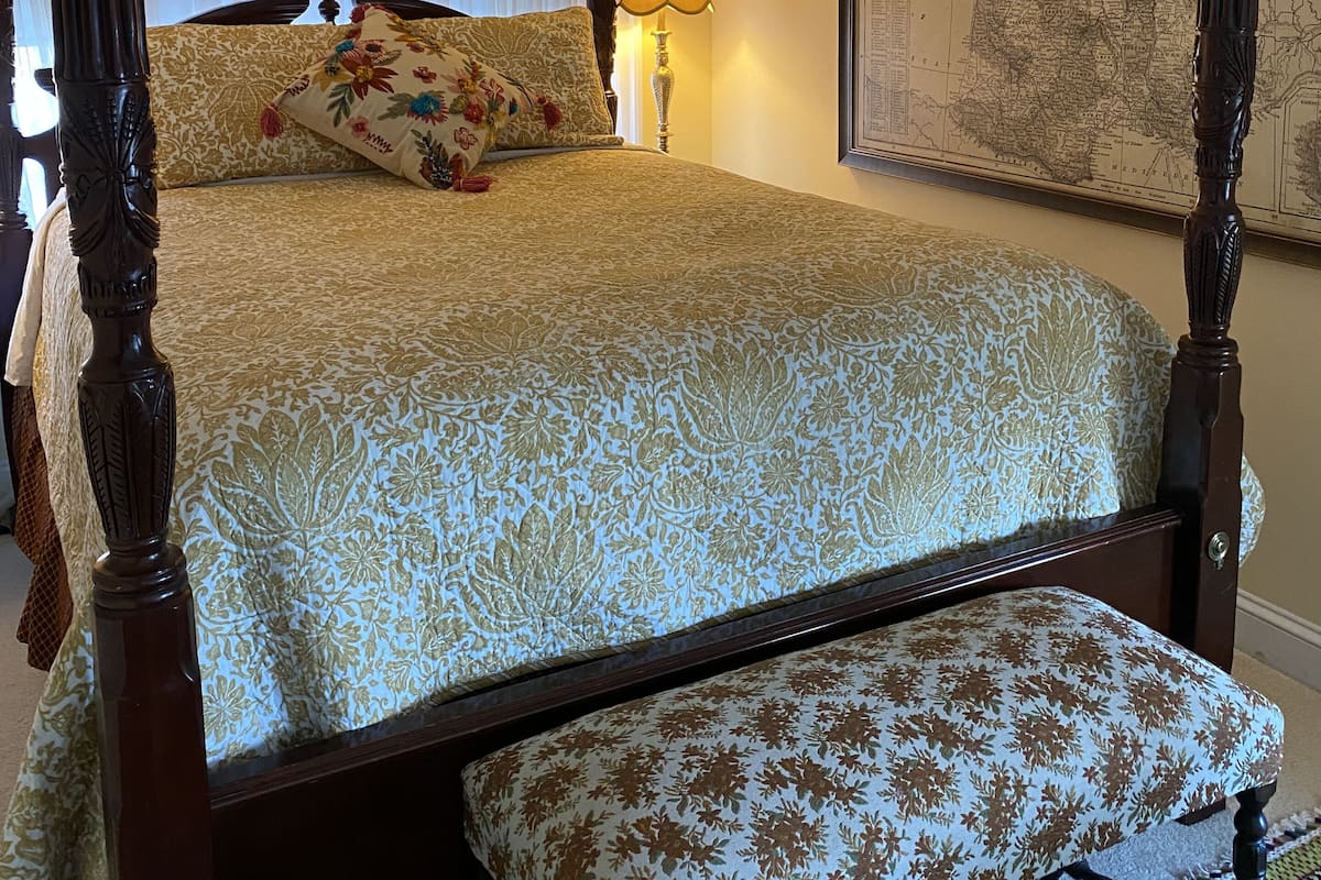 Un lit à baldaquin avec une couvre-lit à motifs floraux, un banc assorti et une carte accrochée au mur.