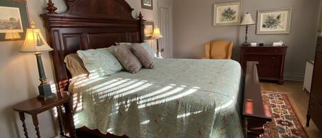 Un dormitorio con una cama grande, cabecera de madera, dos mesitas de noche con lámparas, una alfombra estampada y cuadros en las paredes.