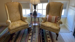 A room with two armchairs, a small round table, a lamp, and a patterned rug. - Inn at 605 (Williamsburg)