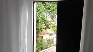 Ein Zimmer mit einem Bett, einem Vorhangfenster und Blick auf Grün.