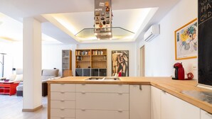 A modern kitchen with a central island, built-in bookshelves, and a dining area with a red table. - SW Mendoza 20 (Málaga)