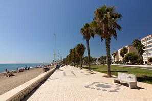 Eine Strandpromenade mit Palmen, Bänken und freiem Blick auf das Meer.