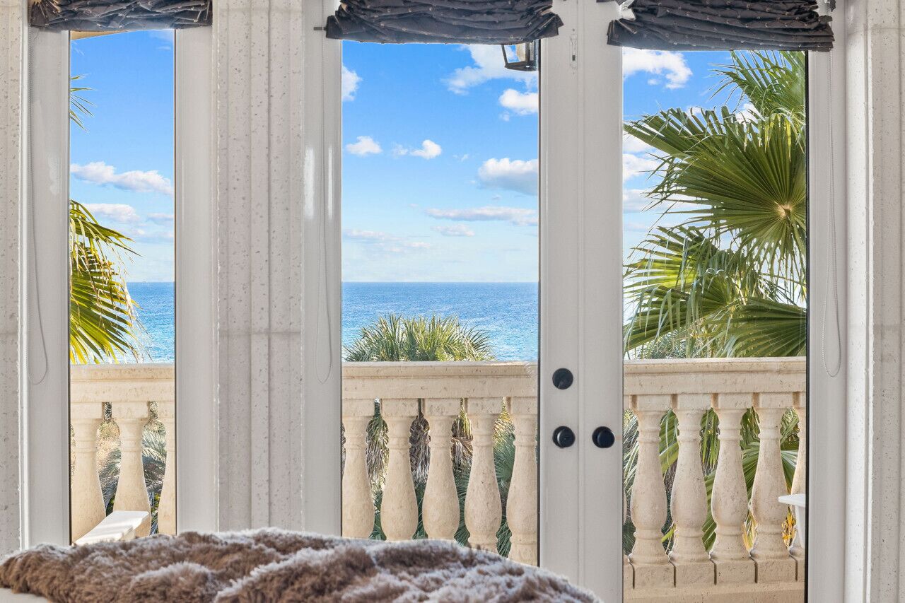 Ein Balkon mit Blick auf den Ozean, weiße Geländer und eine Tür mit strukturierter Verkleidung.