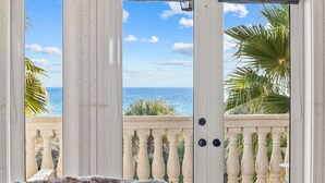 Un balcón con vistas al océano, barandas blancas y una puerta con revestimiento texturizado.