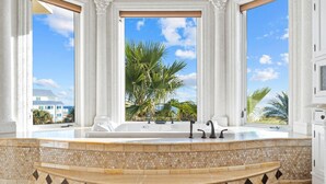 Un baño lujoso con una bañera independiente, ventanas amplias y vistas a palmeras.