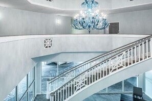Un interior moderno con una escalera de cristal, una araña y vistas de la ciudad.