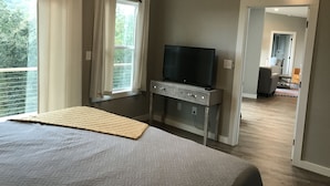 Une chambre à coucher avec un grand lit, un téléviseur posé sur un meuble et une vue sur l’extérieur par une fenêtre.