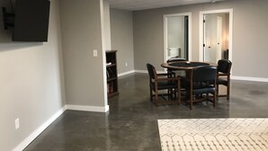 Une pièce comprenant une table à manger, des chaises, une bibliothèque, un téléviseur à écran plat fixé au mur et un tapis à motifs sur le sol.