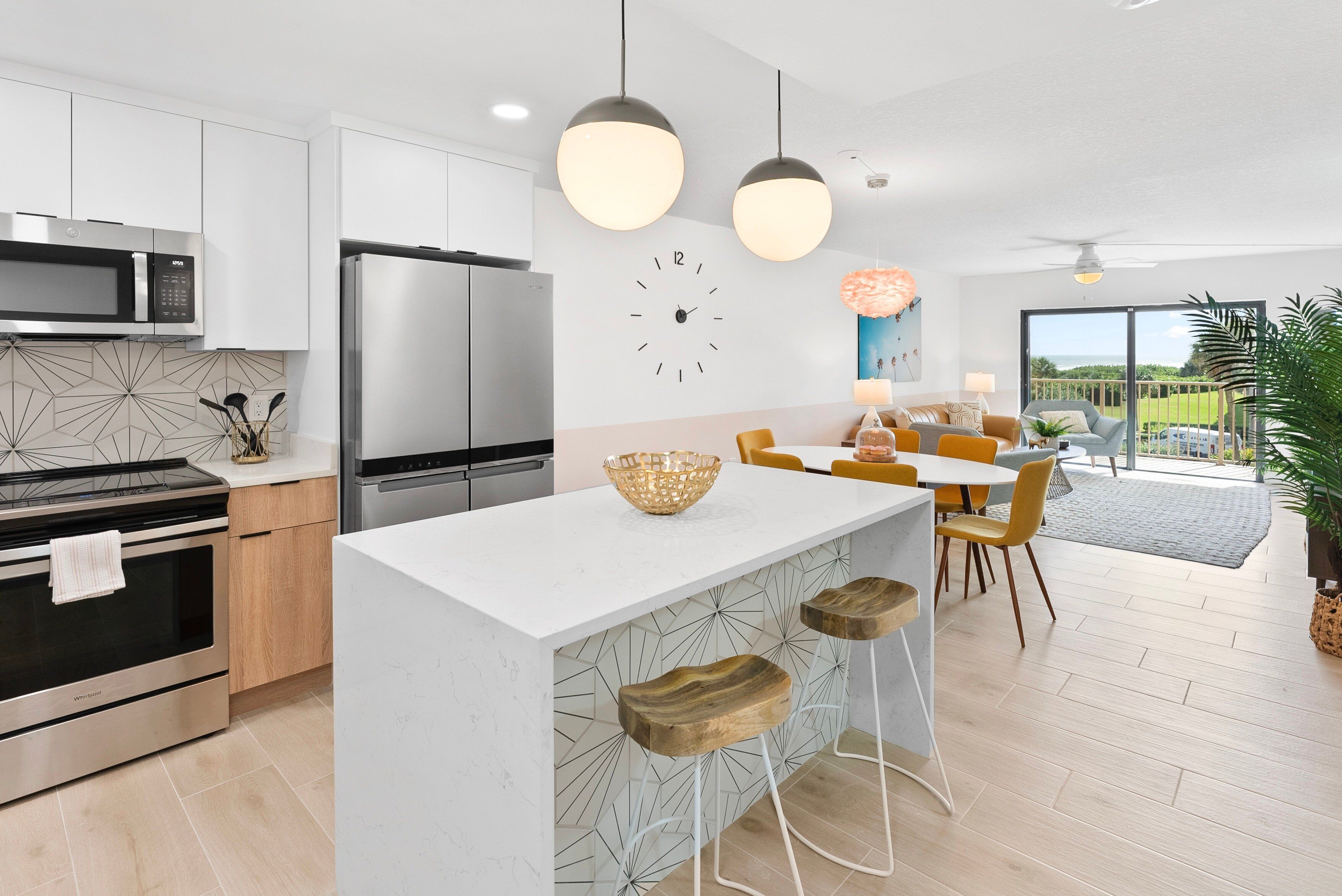 A modern kitchen with stainless steel appliances, a central island with stools, and a dining area with yellow chairs.