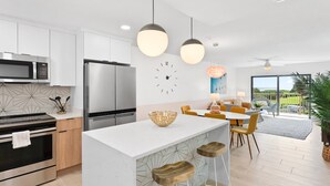Una cucina moderna con elettrodomestici in acciaio inossidabile, un'isola centrale con sgabelli e un'area pranzo con sedie gialle.