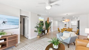 Un soggiorno moderno con una TV a schermo piatto, una ventola a soffitto e un'area pranzo con sedie gialle.