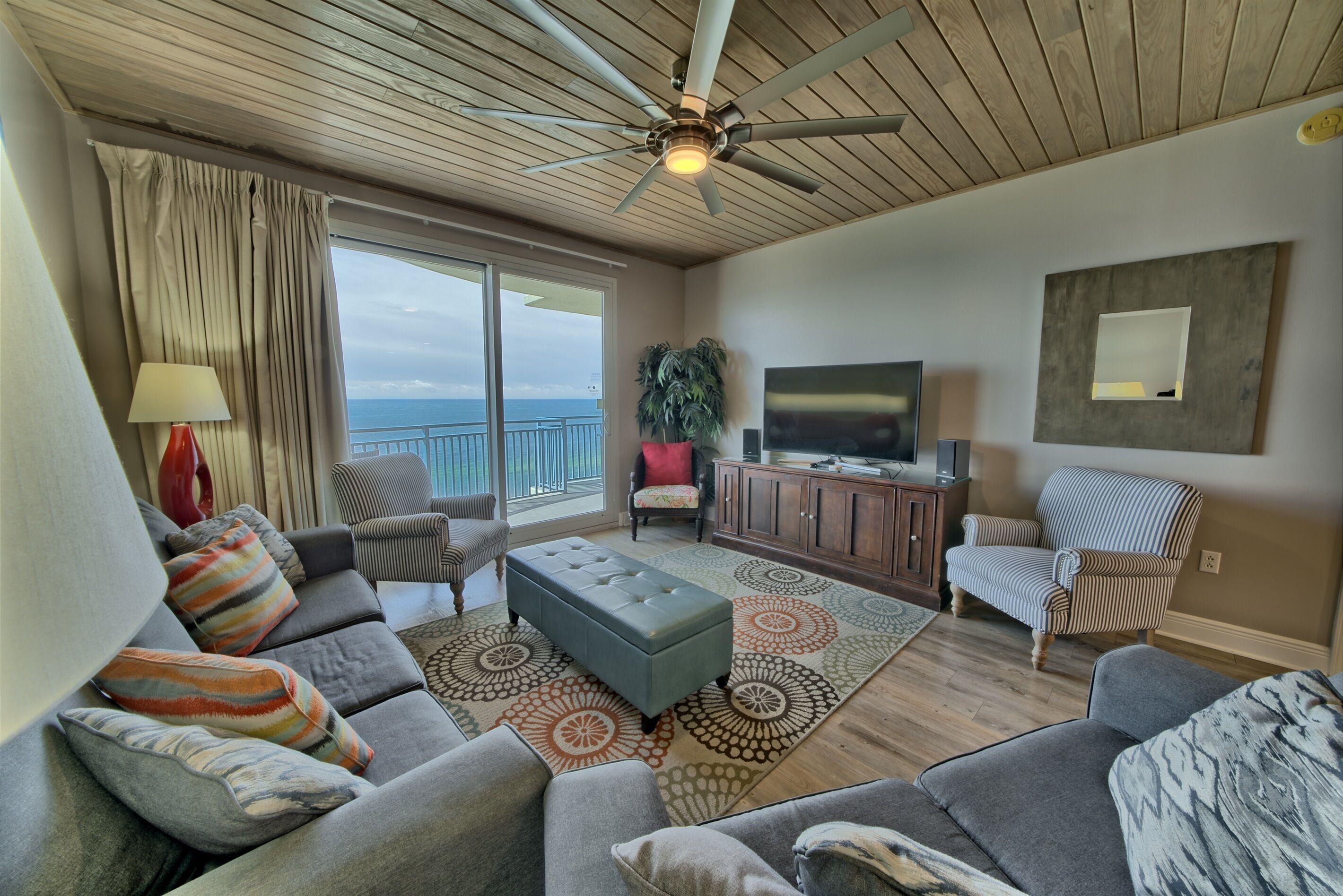 A spacious living room with a ceiling fan, a large TV, and a view of the ocean.