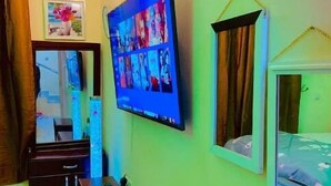 Una habitación con televisión montada en la pared, un espejo, una cama y un aparador.