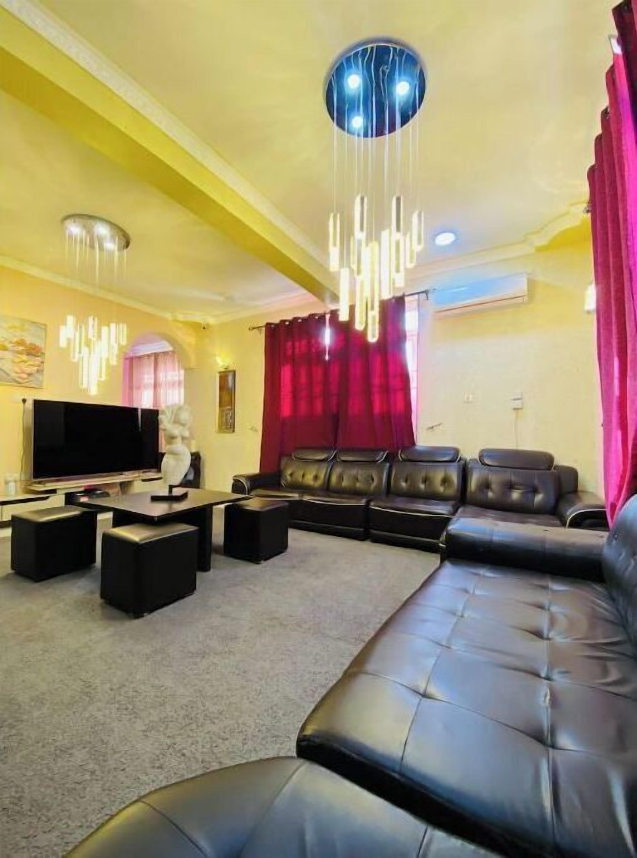 A living room with a large black leather sofa, a flat-screen TV, and modern pendant lighting.