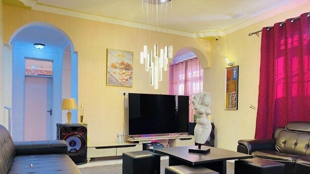Una sala de estar moderna con un sofá de cuero negro, un televisor de pantalla plana, una escultura blanca y una cortina roja.